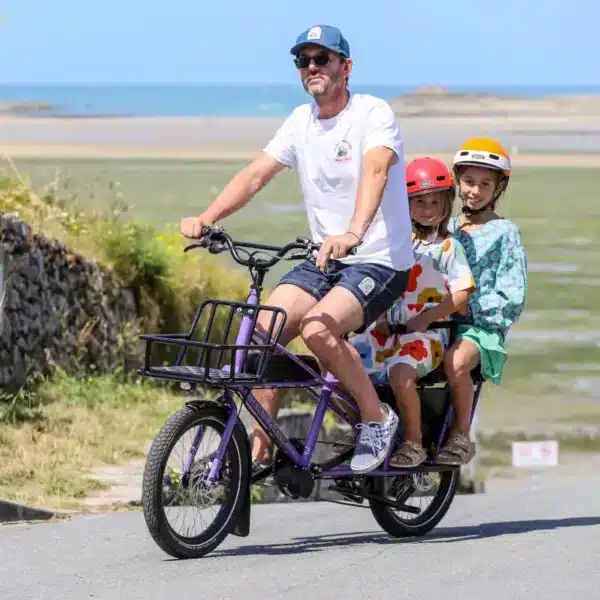 Un homme et ses deux filles sur une petit porteur Longtail électrique en vacances au bord de la mer