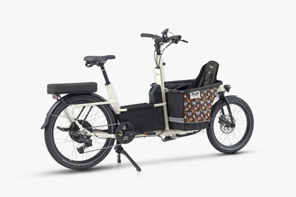 Photo du vélo Shwette Baggy en coloris blanc cassé et équipé de sa caisse de transport avant aux motifs colorée